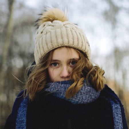 Kind mit beiger Strickmütze mit Bommel und blauem Schal im winterlichen Wald – Alpaka-Mütze „Bergwind“