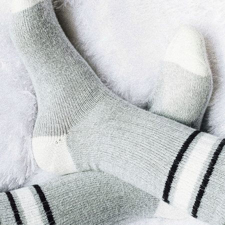 Getragene Alpaka-Socken „Hofklassiker“ in Grau mit weißer Spitze und schwarzen Streifen auf flauschiger Decke